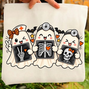 May include: A white canvas tote bag featuring a graphic of three cartoon ghosts dressed as medical professionals. The ghosts hold X-ray images showing a skeletal hand, a rib cage with a heart, and a skull. Orange bows, bats, and hearts surround them.