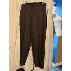 May include: Dark brown dress pants with a button closure and a straight leg. The pants are hanging on a black hanger against a neutral background. The pants appear to be made of a woven fabric.