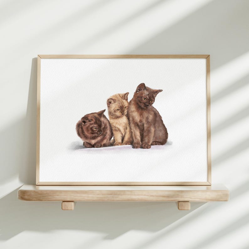 K&ouml;nnte beinhalten: Ein gerahmter Kunstdruck mit einer detaillierten Illustration von drei zusammen sitzenden K&auml;tzchen. Zwei K&auml;tzchen sind dunkelbraun und ein K&auml;tzchen in der Mitte ist hellbeige. Das Kunstwerk befindet sich in einem einfachen, hellen Holzrahmen.