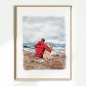 May include: Watercolour painting of a person in a red jacket with a golden retriever dog, sitting on a sandy beach, looking out at the ocean under a cloudy sky. The artwork is framed in a light wood frame.