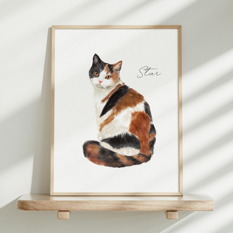 K&ouml;nnte beinhalten: Ein gerahmter Aquarelldruck eines dreifarbigen Katzenbildes mit schwarzem, orangefarbenem und wei&szlig;em Fell, das sitzt und den Betrachter ansieht. Die Katze hat bernsteinfarbene Augen und eine rosa Nase. Rechts neben der Katze steht das Wort Star in schwarzer Schreibschrift.