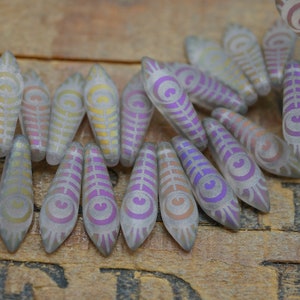 May include: A collection of iridescent glass beads with a feather design. The beads are clear with a subtle purple and gold iridescent sheen.