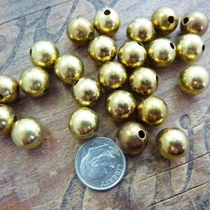 May include: A pile of 20 gold-colored metal beads with a hole through the center. The beads are about the size of a US dime.