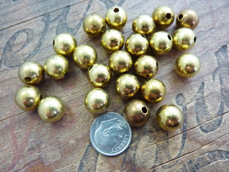 May include: A pile of 20 gold-colored metal beads with a hole through the center. The beads are about the size of a US dime.