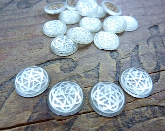 May include: A collection of clear glass buttons with a white, intricate, floral design. The buttons are round and have a slightly raised edge.