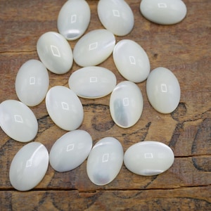 May include: A collection of oval-shaped, white mother of pearl cabochons. The cabochons are smooth and have a slight iridescent sheen.