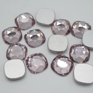 以下が含まれることがあります： 銀色の裏地が付いた薄いピンク色の正方形のラインストーンの詰め合わせ。