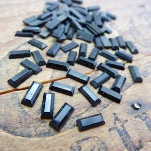 May include: A large quantity of black rectangular rhinestones, scattered on a wooden surface.