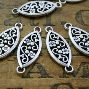 May include: Silver oval-shaped connector charms with a floral design. Each charm has two jump rings for attaching to jewelry or other crafts.