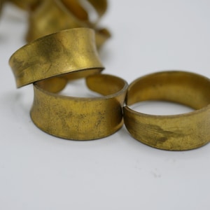 May include: A set of three gold-toned metal rings, each with a slightly different shape and width. The rings are stacked on top of each other, with the largest ring on the bottom and the smallest ring on top.