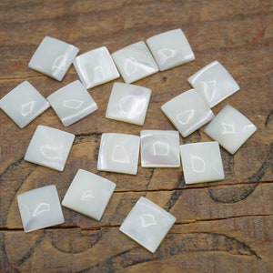 May include: A collection of 15 white mother of pearl tiles, each with a unique, natural pattern. The tiles are square and have a smooth, polished surface.