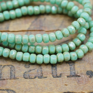 May include: A strand of turquoise blue glass beads with a slightly textured finish. The beads are small and square-shaped.
