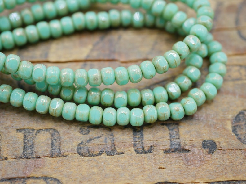 May include: A strand of turquoise blue glass beads with a slightly textured finish. The beads are small and square-shaped.