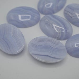 May include: A collection of oval-shaped, pale blue gemstones with swirling patterns. The polished stones have a smooth, glossy surface and vary slightly in their color and veining. These stones are likely used for jewelry or crafts.