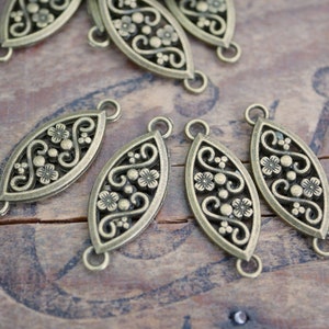 May include: Antique brass oval connector charms with a floral design. The charms have two jump rings on each side.