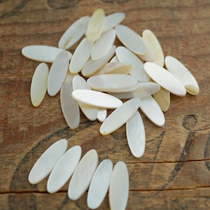 Op de afbeelding: Een stapel witte ovale stukjes parelmoer op een houten oppervlak.