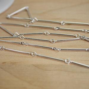 May include: A silver chain necklace with a unique bar link design. The chain is made of small, thin bars connected by small, round rings.