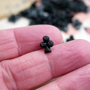 May include: A black plastic charm in the shape of a playing card club symbol.