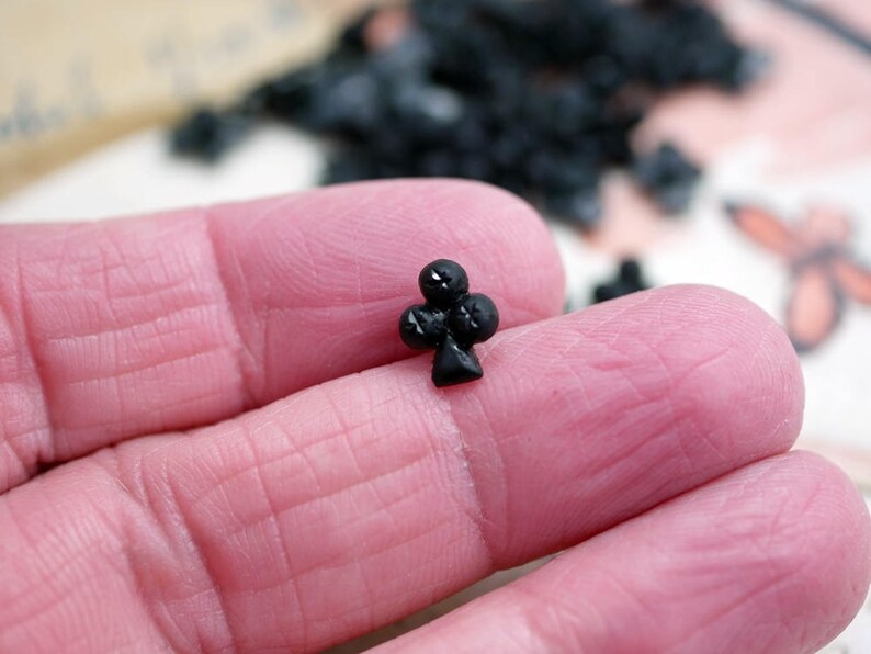 May include: A black plastic charm in the shape of a playing card club symbol.