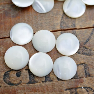 May include: A collection of white mother of pearl round buttons. The buttons are smooth and shiny.