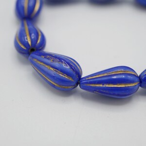 May include: A strand of blue glass beads with gold accents. The beads are teardrop shaped and have a ribbed texture.
