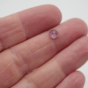 Op de afbeelding: Een kleine, ronde, roze edelsteen met een licht onregelmatige vorm.