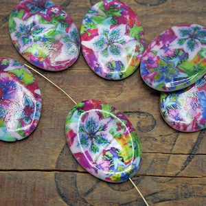 May include: Six oval-shaped ceramic beads with a white background and a colorful floral pattern. The beads are glossy and have a pink, blue, green, and yellow color scheme.
