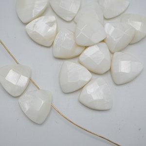 May include: A collection of white triangular shaped mother of pearl beads. The beads have a faceted, iridescent finish.
