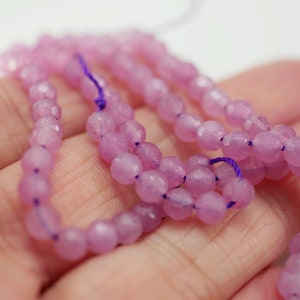 May include: A strand of light pink faceted gemstone beads. The beads are strung on a purple thread.