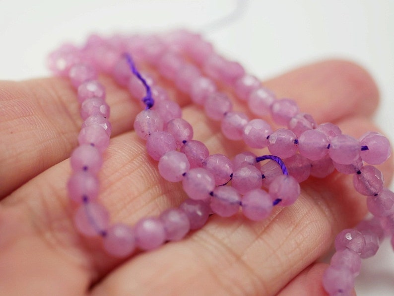 May include: A strand of light pink faceted gemstone beads. The beads are strung on a purple thread.