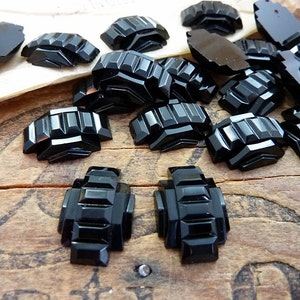 Peut inclure: Une collection de cabochons en verre noir, g&eacute;om&eacute;triques et facet&eacute;s. Les cabochons sont dispos&eacute;s sur une surface en bois.