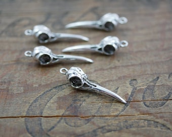 May include: Five silver bird skull charms with a detailed design. The charms have a loop at the top for attaching to jewelry or other crafts.