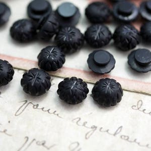 May include: A collection of black glass buttons with a starburst design. The buttons are arranged on a piece of paper with handwritten text.
