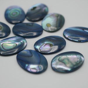 May include: A collection of ten oval-shaped iridescent blue abalone shell cabochons. The cabochons have a smooth, polished surface and a variety of blue, green, and purple hues.