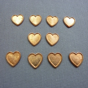 May include: Ten gold-coloured heart-shaped metal charms. The charms are all the same size and shape, and they have a slightly textured surface.