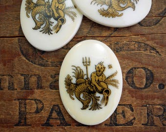 May include: White oval ceramic tile with a gold illustration of the astrological sign Aquarius. The illustration depicts a mythical creature with a human torso and a fish tail holding a pitcher of water.