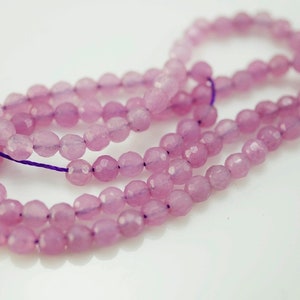 May include: A strand of light pink faceted gemstone beads. The beads are strung on a purple thread.