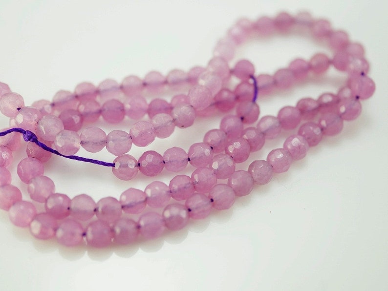 May include: A strand of light pink faceted gemstone beads. The beads are strung on a purple thread.
