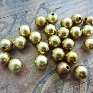 May include: A group of 20 gold-colored metal beads with a hole through the center. The beads are round and smooth.