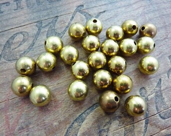 May include: A group of 20 gold-colored metal beads with a hole through the center. The beads are round and smooth.