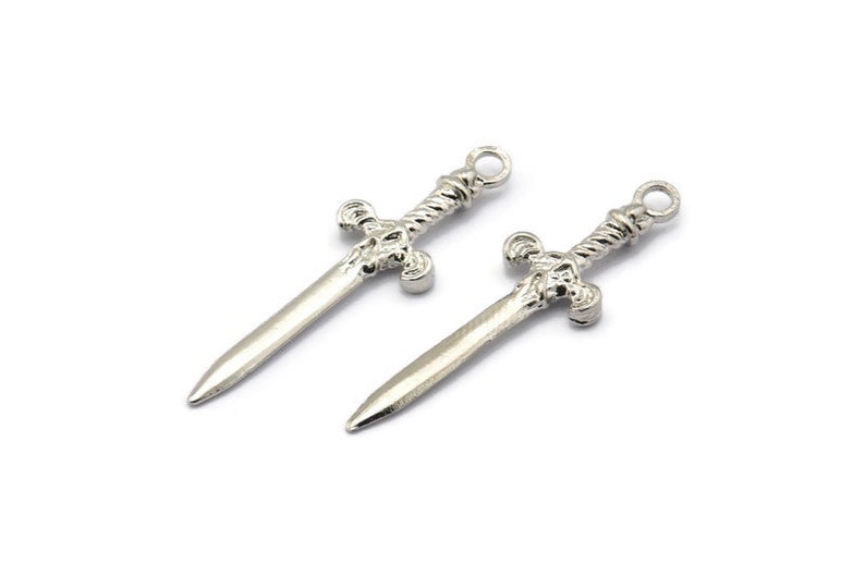 May include: Two silver sword charms with intricate details. The swords have a twisted design and a cross-shaped hilt.
