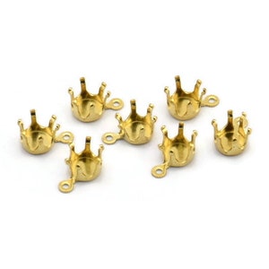 May include: Seven gold-tone metal crown-shaped settings with a loop on the side. The settings are designed to hold a gemstone or other embellishment.