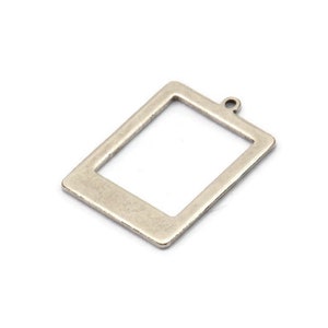 Puede incluir: Un dije rectangular de metal plateado con un centro hueco y un pequeño lazo en la parte superior. El dije tiene un acabado ligeramente desgastado, lo que sugiere una estética antigua o vintage. Ideal para la fabricación de joyas o proyectos de artesanía.