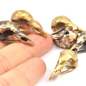 May include: Five small, gold-colored metal bird skull charms. The skulls are detailed and have a textured finish.