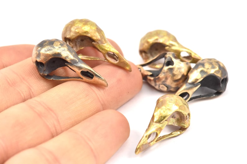 May include: Five small, gold-colored metal bird skull charms. The skulls are detailed and have a textured finish.