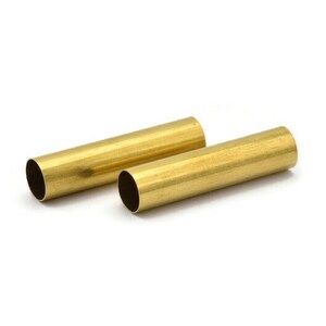 Könnte beinhalten: Zwei goldfarbene Metallrohre, jedes mit einer glatten, zylindrischen Form. Die Rohre liegen nebeneinander auf einer weißen Oberfläche.