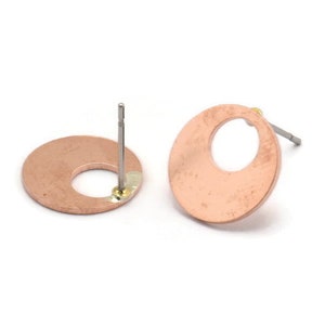 Könnte beinhalten: Ein Paar Ohrstecker aus Kupfer mit einem runden Design und einem kleinen Loch in der Mitte. Die Ohrringe haben eine gebürstete Oberfläche und sind an silbernen Stiften befestigt.