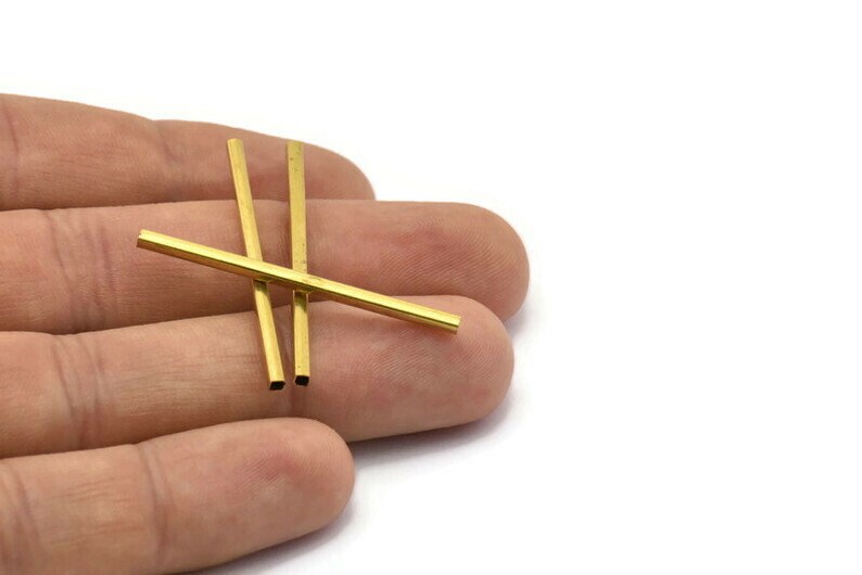 May include: Three gold-coloured metal tubes, approximately 3.8 cm long, are lying on a hand. The tubes are square in cross-section.