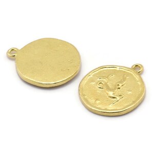 Op de afbeelding: Twee goudkleurige metalen bedels, een met een blanco ronde zijde en de andere met een reli&euml;f van een geit of ram. Beide bedels hebben een lus om aan een ketting of armband te bevestigen.