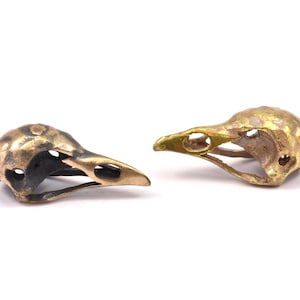 May include: Two small bird skull charms, one with a gold finish and the other with a black finish.
